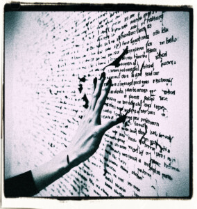 Picture of a long and selnder hand with black fingertips seemingly spreading words from the fingertips.