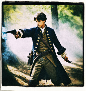 Teenage boy in the woods firing flintlock pistol as though in a duel, including smoke and fire from the gunfire. Clothes and background appropriate for 16th century France.