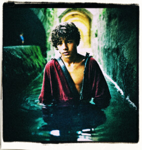 Teenage boy with a dislocated shoulder pulling himself out of the water in a dark tunnel. Clothes and background appropriate for 16th century France.