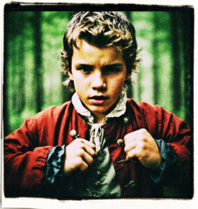 Boy of French decent, in the woods, is angry. His eyes narrowed, jaw clenched, fingers formed into fists, veins bulging from neck and forehead, red faced. Clothes and scene appropriate for 1600s France.