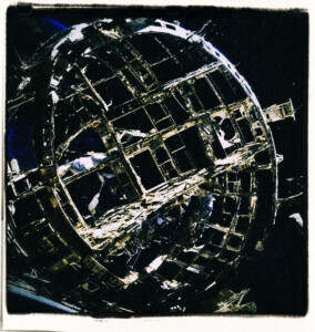 Picture of a cicular space station with several sections visibly damaged, debris floating through space, and the earths pale shadow in the distance.