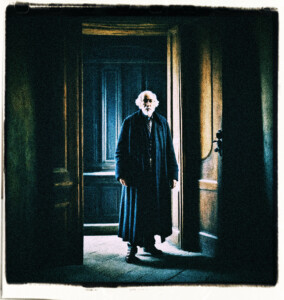 Picture of doctor, a tall, thin, old man. His face frozen in horror of what he sees. By an open door in a dark castle hall. Clothes and background appropriate for 16th century France.