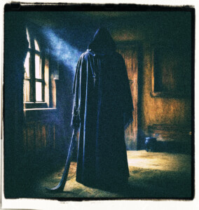Grim reaper with a long cloak and a long implement at their side looking away from the camera. Appears to be in a dark bedroom with light filtering through a window.