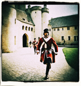 Guard running into the courtyard of a castle to deliver the message. Castle staff go about their day. Background and clothing appropriate to 16th Century France.