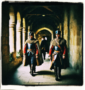 Two guards marching down the hallway of a stone keep. Clothes and style appropriate for 16th century France.