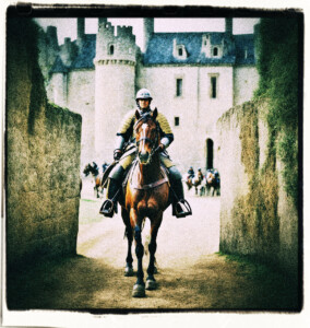 A French soldier riding a riding a warhorse. He face two armed guards at the gate of a castle. Background and clothing appropriate to 16th Century France.