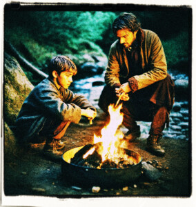 An man in his forties and a boy sitting by a campfire. The man is stoking the fire, while the boy stares into the fire. Both are wet from falling in a nearby creek. Clothes and scene appropriate for 1500s France.