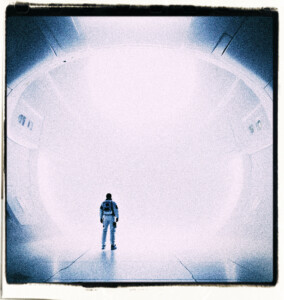 Picture of a man in a space suit facing a large white surface. So bright that it appears to glow. 