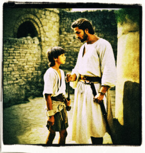 Picture of a man talking to a boy, in a remote area of a keep.