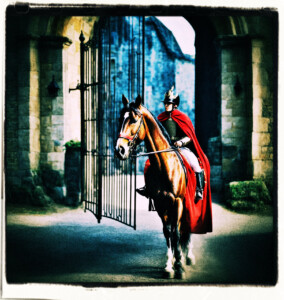 Horse and rider coming to a hard stop, wearing the kings colors at the castle gates. Background and scene appropriate to 16th century France.through the gates