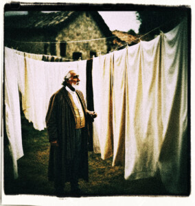 Old noble man speaking looking at white sheets hanging on a clothes line. Background and clothing appropriate to 16th Century France.