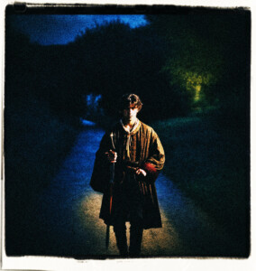 A young noble faced by a shadowy figure holding a sword. On a road in the dark books lit by the moonlight only.Scene and clothes appropriate for 16th century France.