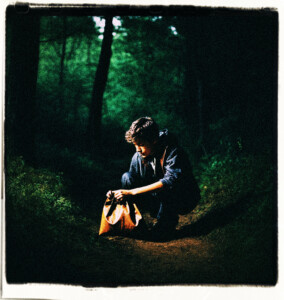 Teenage boy rummaging through a leather pouch for something. Boy is in the dark woods at night, near a dusty road. Scene and clothes appropriate for 16th century France.