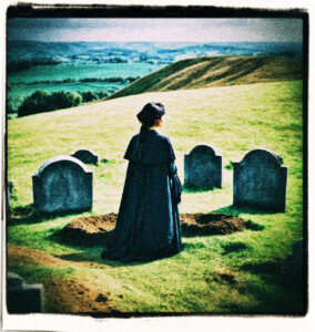 A grieving woman dressed in black standing besides a freshly dug grave. Grave site is on a hill. Clothes and scene appropriate for 1500s France.