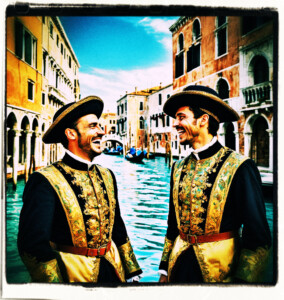 Two servants in uniform laughing at the expense of a nearby guest. Clothes and setting appropriate to 16th century Venice