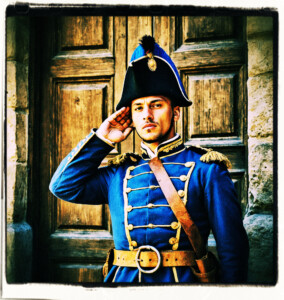 A soldier saluting by an open door. Scene and clothing appropriate for 16th century France.