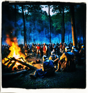 Night shot from high of campfires and scores of soldiers sitting around them in the woods. Scene and clothing appropriate for 16th century France.