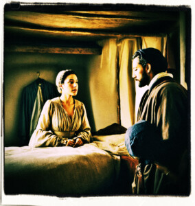 Woman lecturing a man in a small simple bedroom. Clothing and setting appropriate for 16th century France.