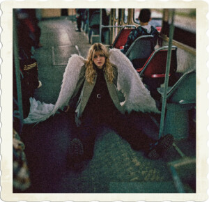 Picture of a blonde on a bus wearing black shirt, pants, and boots with a grey jacket and white wings. Sitting on the floor of a city transit bus. Image by Anastasiia Shevchenko from Pexels.