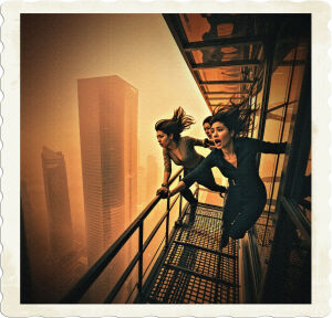 A dramatic, high-contrast cinematic photo of three women, each with unique facial features and skin tones, clinging to the railing of a window cleaning platform as it precariously sways outside a sleek, modern high-rise building, the foggy orange haze enveloping the city skyline and blocking out the sun, casting an eerie, diffused light, with the women's clothing and hairstyles blown back by the wind, their expressions a mix of fear and determination, the platform's metal latticework and the building's glass and steel exterior reflecting the warm, golden tones of the fog, with a shallow depth of field to emphasize the tension and vulnerability of the moment, photographed in a horizontal format with ample negative space to convey the sense of height and isolation.